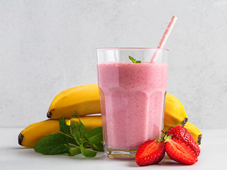 Un smoothie roz cu căpșuni și banane, decorat cu mentă, pe o masă albă.