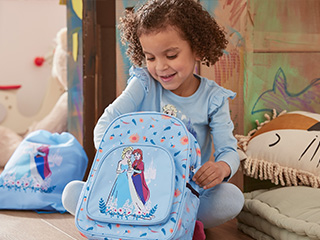 O fetiță zâmbitoare ține un rucsac Frozen, cu o geantă asortată în fundal.