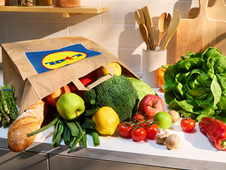 O pungă de cumpărături Lidl plină cu fructe și legume proaspete pe un blat de bucătărie.