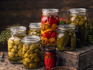 Borcane de sticlă cu legume murate, inclusiv castraveți, ardei și măsline.