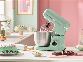 Un mixer de bucătărie verde mentă pe un blat, cu ingrediente de copt și un tort decorat.