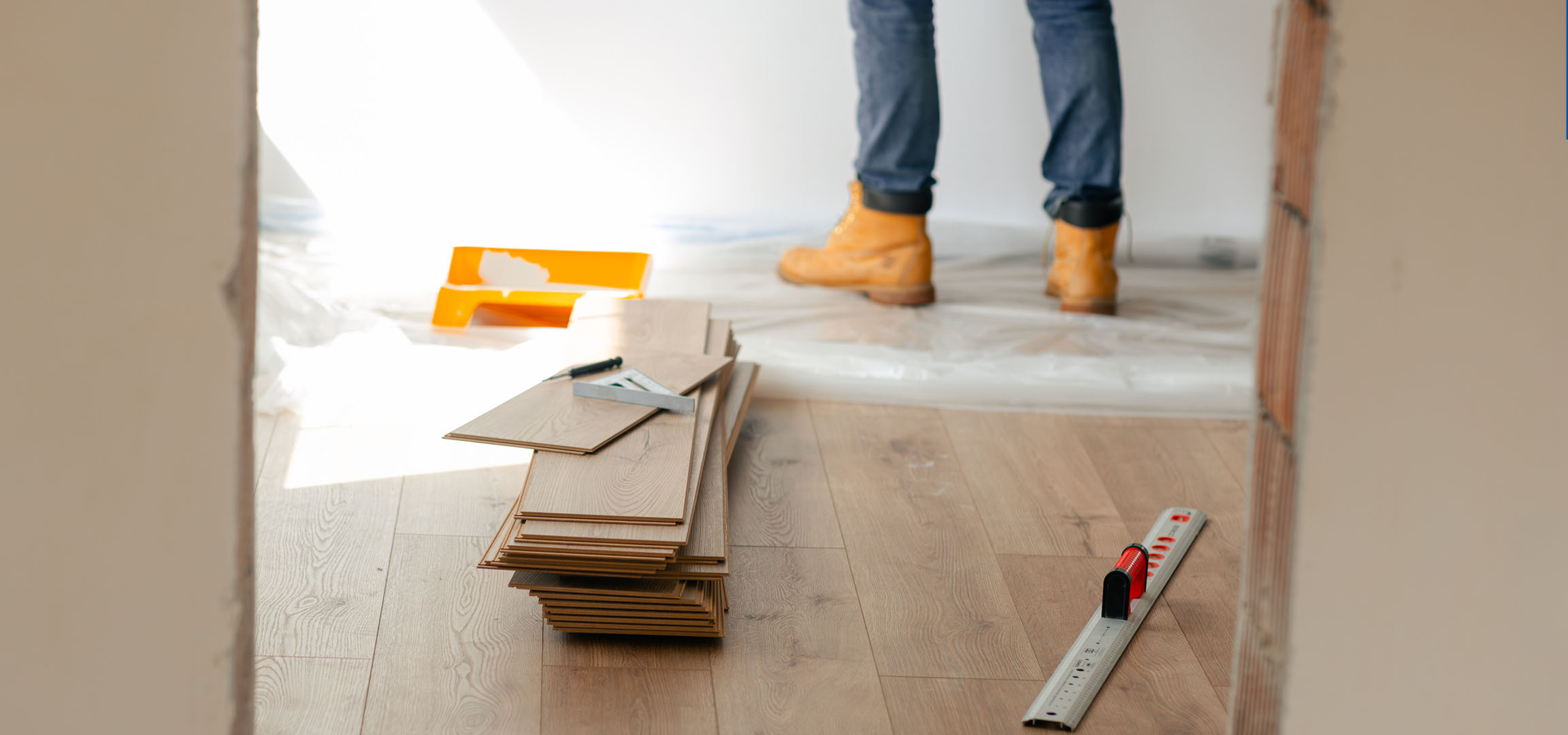Plăci de parchet laminat și unelte de instalare pe o podea de lemn, cu o persoană în cizme.