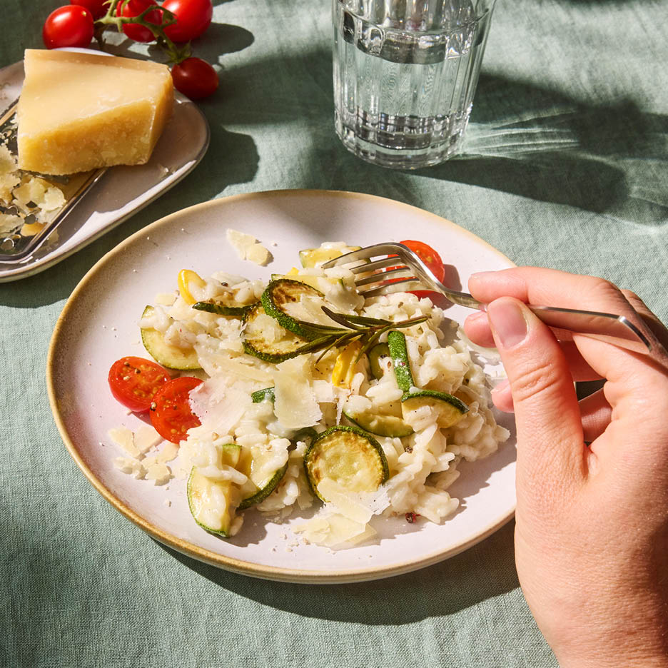 Risotto cu dovlecei, roșii cherry și parmezan, cu o mână care ține o furculiță.