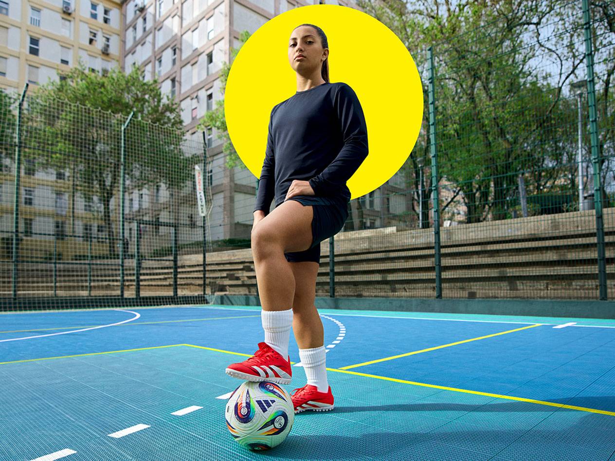 Jucătoare de fotbal cu adidași Adidas pe un teren albastru.